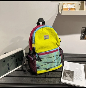 Detail of color-block backpack with elastic bungee net and brand label on wood surface