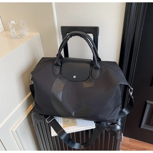 Detail of a large black travel tote bag with leather handles resting on a suitcase