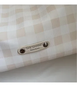 Détail de la texture à carreaux vichy beige avec plaque logo en métal doré ovale