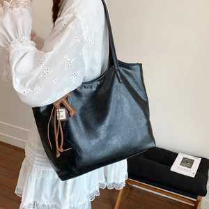 Detalle de un bolso tote grande de cuero negro con colgante en T marrón sobre el hombro