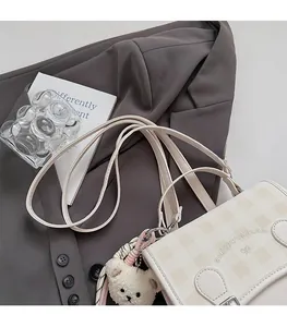 Detail of checkered shoulder bag with cute plush bear charm and bow logo on blazer