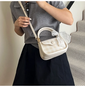 Detail of cream crossbody bag featuring checkered flap and delicate white lace bow charm