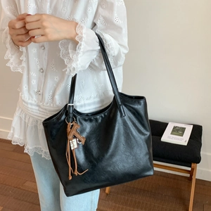Detalle de bolso tote de cuero negro con un colgante de perrito marrón para diario