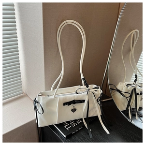 Detail view of white shoulder bag featuring a black bow and heart-shaped metal pendant