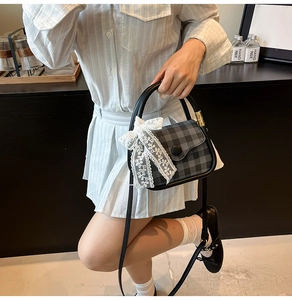 Detail of grey plaid crossbody bag with lace bow and round buckle on a textured model
