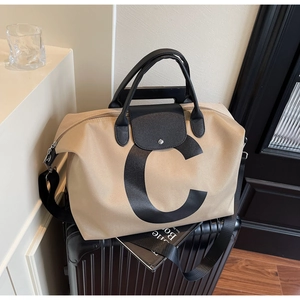 Close-up of beige travel tote bag with black leather handles on a black suitcase