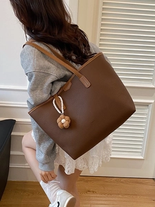Sac fourre-tout marron avec breloque perle porté par un mannequin dans une pièce chic
