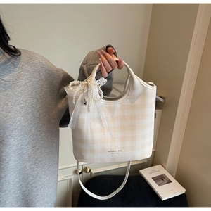 Detail of checkered tote bag with lace bow, pearl charm, and heart pendant accessory