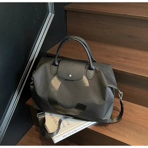 Detail of black large travel tote showing textured leather flap and metallic snap closure