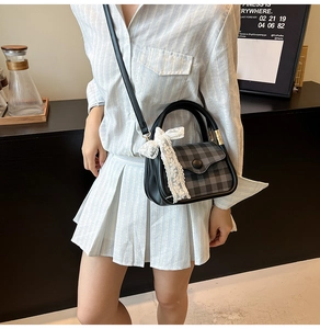 Detail of grey plaid handbag with white lace bow and black button on the flap