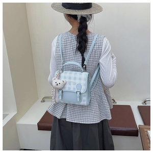Gros plan du mini sac à dos à carreaux avec boucles argentées et breloque ours en peluche