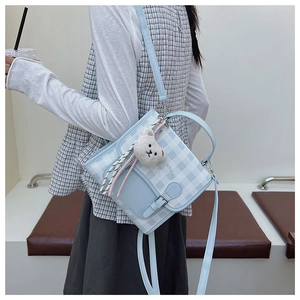 Vue détaillée du sac à bandoulière à carreaux bleus avec un pendentif ours en peluche