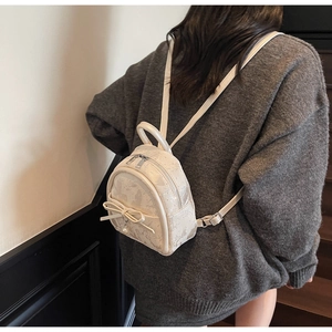 Detail view of mini cream PU backpack with bow and pearl pendant on a model's back