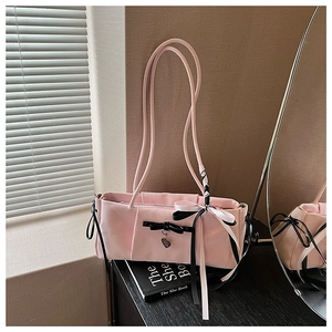 Detail of pink shoulder bag featuring black bows and heart pendant in a chic setting