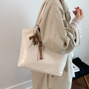 Detalle del bolso tote blanco crema con colgante de letra T marrón y borla en el lateral