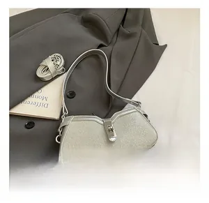 Detail shot of a silver glitter baguette bag with a sleek metal clasp on a grey blazer