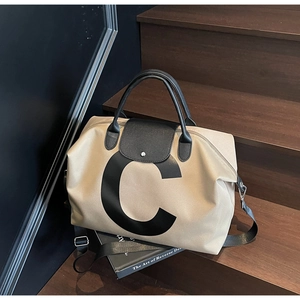 Detailed view of beige travel tote bag with large letter C and black leather handles