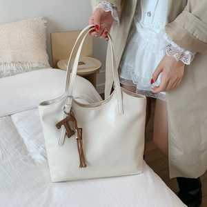 Detalle del bolso tote de cuero PU blanco crema con colgante de borla marrón y dije en T
