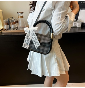 Close-up of black and grey checkered handbag featuring white lace bow and round handle
