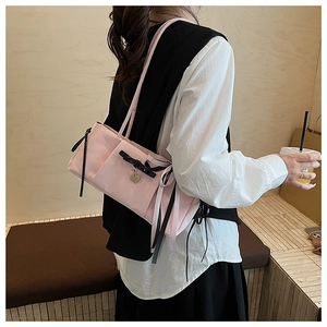Pink shoulder bag with black bow ribbon and gold heart tag detail on a model