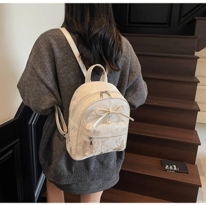 Close-up of a cream bow backpack with pearl charm worn on a wooden staircase