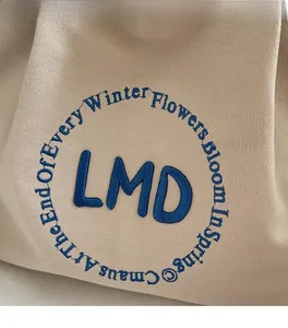 Close-up of beige canvas tote with navy blue LMD embroidery and textured fabric detail