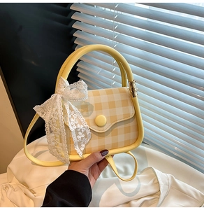Macro detail of yellow checkered handbag featuring a white lace bow and smooth fabric texture