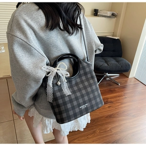 Detailed shot of dark plaid Boston bag featuring white lace bow and pearl pendant charm