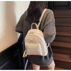 Close-up of beige mini backpack with bow and pearl detail worn by model on stairs