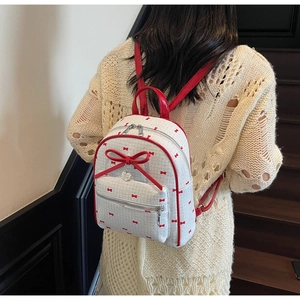 Close-up of a white backpack featuring red bow patterns and a heart-shaped pendant detail