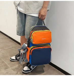 Detail of multi-pocket patchwork backpack in blue and orange with plush charm