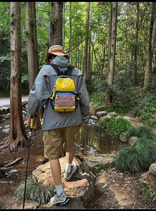 Outdoor hiker using a vibrant yellow color-block backpack by a forest stream