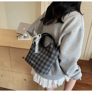 Detail of plaid tote bag featuring a pearl charm and lace bow on a black leather handle
