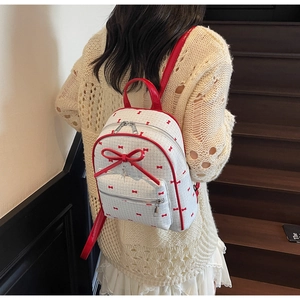 Close-up of small white backpack with red bow patterns and 3D bow detail worn by model