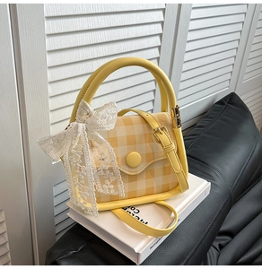 Detail of yellow checkered crossbody bag with oversized white lace bow and round handle
