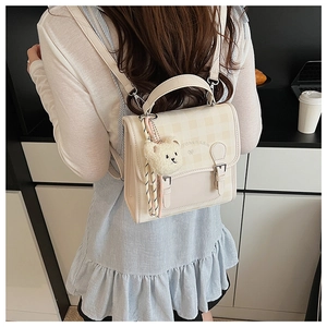 Détail du mini sac à dos crème à carreaux avec breloque d'ours sur une femme