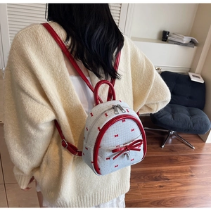 Detailed view of white mini backpack with red bow print and glossy patent leather trim