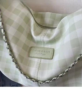 Close-up of light green plaid fabric texture with leather logo tag and metal chain strap