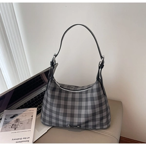 Détail d'un sac hobo à carreaux gris avec bandoulière en cuir sur un bureau minimaliste