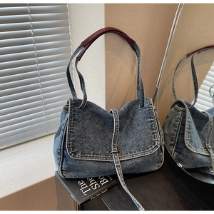 Close-up of vintage denim tote bag with white stitching and burgundy leather handle