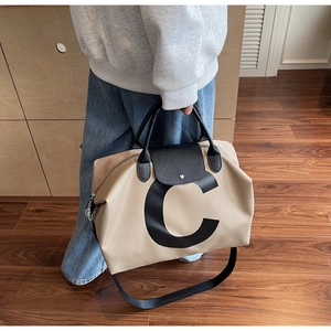 Detail of a beige canvas travel tote with black leather flap and printed letter C