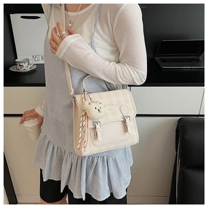Detail of plaid beige crossbody bag with cute bear charm and tassel on city backdrop