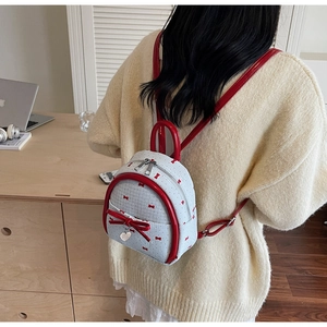 Close-up of a white mini backpack with red bow patterns and a heart metal pendant