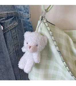 Close-up of a cute white plush bear charm hanging on a green checkered crossbody bag