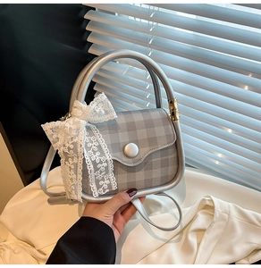 Detail of silver plaid handbag featuring large white lace flower bow and metallic handle
