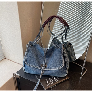 Detailed close-up of denim shoulder bag with metal buckle and contrast wine red handle