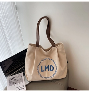 Detail of canvas tote bag featuring premium leather straps and blue circular embroidery