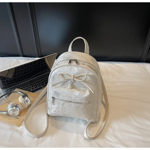 Detail view of cream backpack with bow and pearl charm on white bedsheets