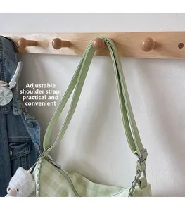 Close-up of adjustable strap and lamb charm on a light green plaid shoulder bag