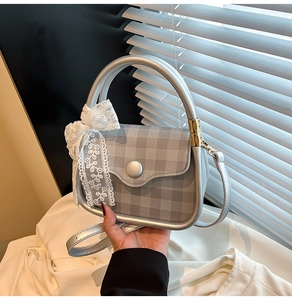 Detail of silver grey plaid handbag featuring a white lace bow charm and golden metal hardware